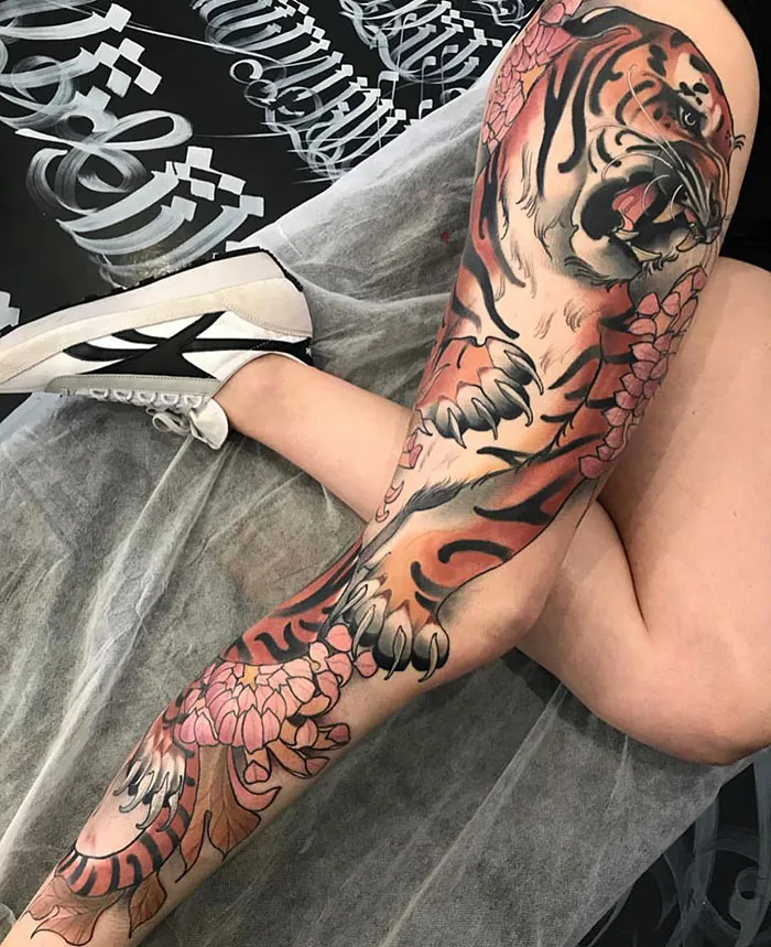 Intricate tiger leg sleeve tattoo with floral accents on a person's leg, showcasing bold design and vibrant colors.