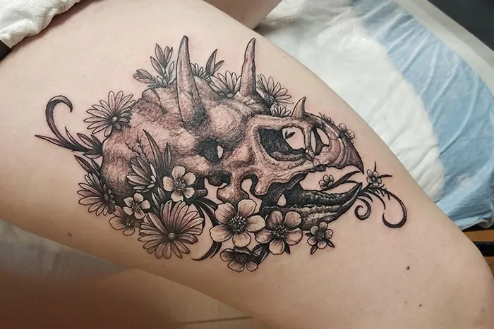 Triceratops skull leg sleeve tattoo with flowers.
