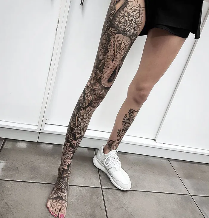 Woman with intricate leg sleeve tattoos featuring elephant and floral designs, wearing white sneakers.