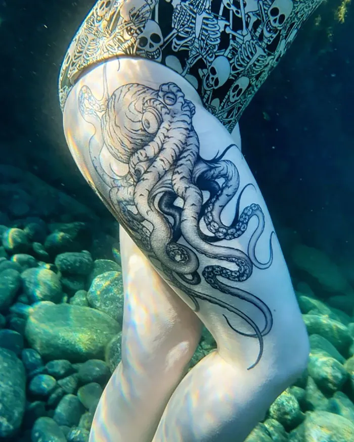 Underwater view of an octopus leg sleeve tattoo on a person's thigh, showcasing intricate design and shading.