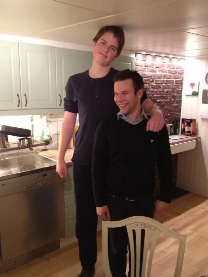 Tall person standing next to a shorter friend in a kitchen, highlighting everyday struggles of tall people in funny situations.