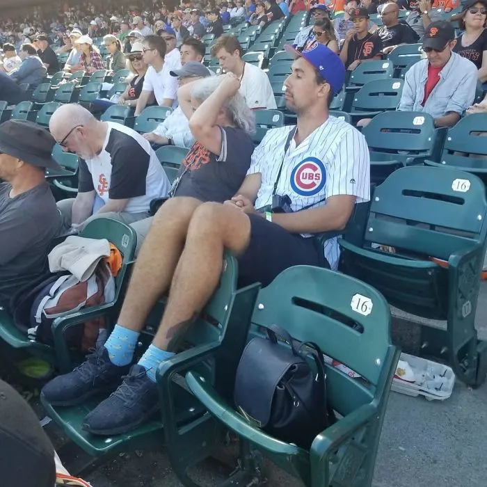 Tall person sitting with legs stretched over two stadium seats, showing common struggles of tall people in public seating.
