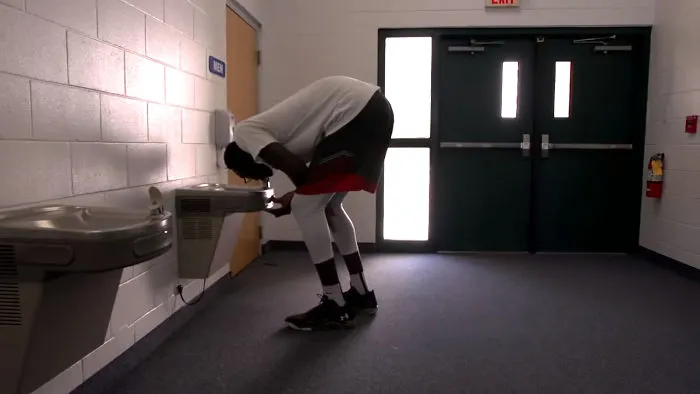 Tall person bending awkwardly to drink from a low water fountain in a hallway, showcasing everyday struggles of tall people.