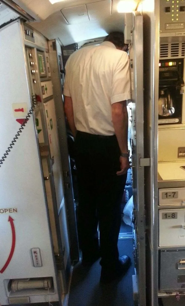 Tall man struggling to fit in a narrow airplane cockpit doorway, illustrating everyday struggles of tall people.