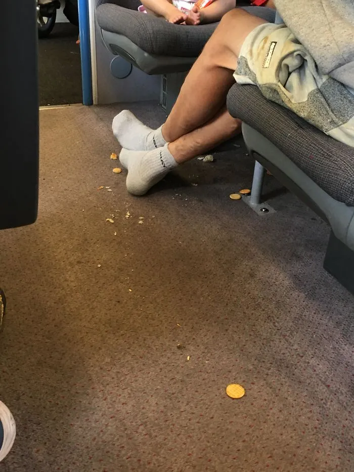 Padre dejando que su bebé tire la comida al suelo del tren y luego pisándola con sus calcetines