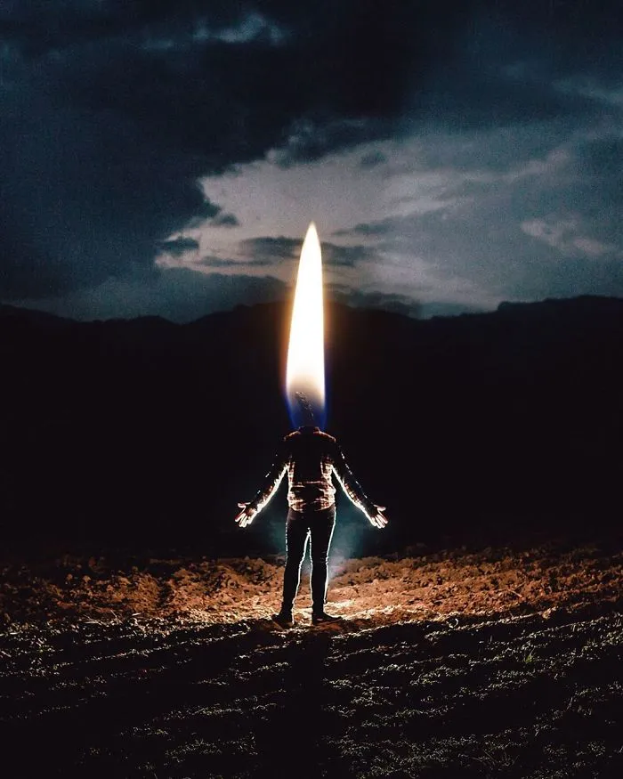 Surreal photo of a person standing in a field with a large flame as their head, creating a visual metaphor.