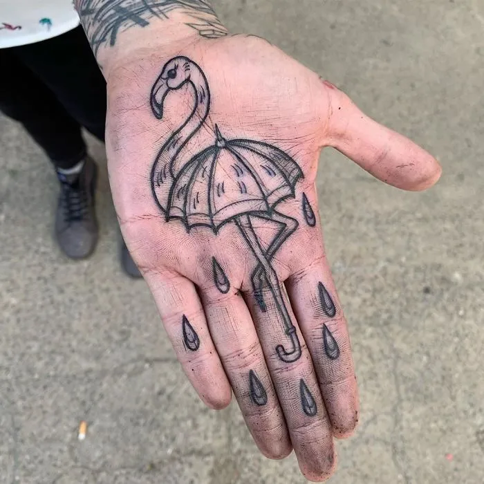 Close-up of a palm tattoo featuring a flamingo and umbrella design, complete with raindrop details.