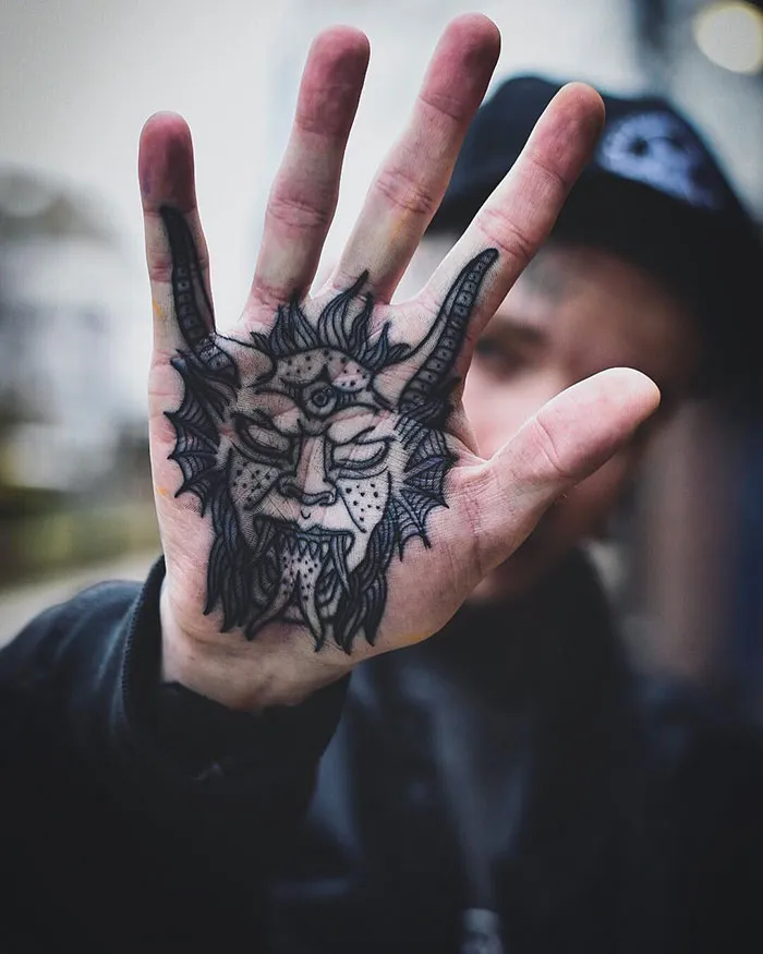Close-up of an intricate palm tattoo design featuring a detailed mythical creature with horns and a third eye.