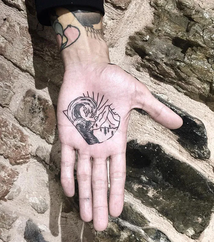 Hand with detailed palm tattoo featuring mountains and waves.