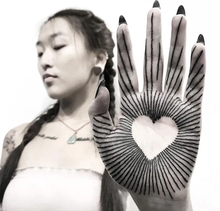Woman displaying a palm tattoo with a heart and radiating lines.