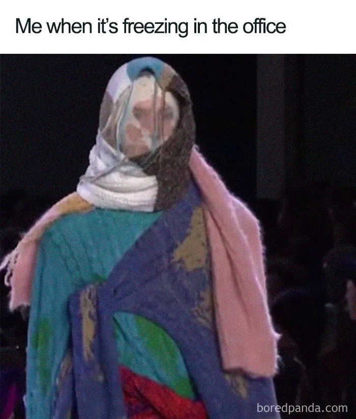 Person wrapped in multiple colorful blankets, humorously depicting freezing conditions in an office.