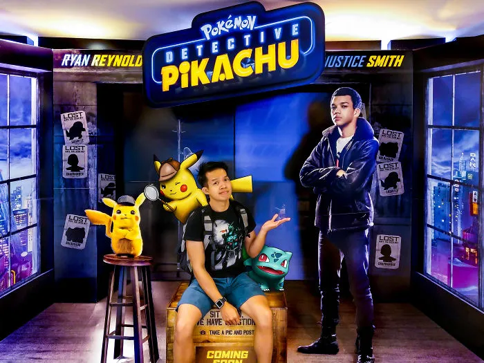 Man posing with Pokémon illustrations at a Detective Pikachu display.