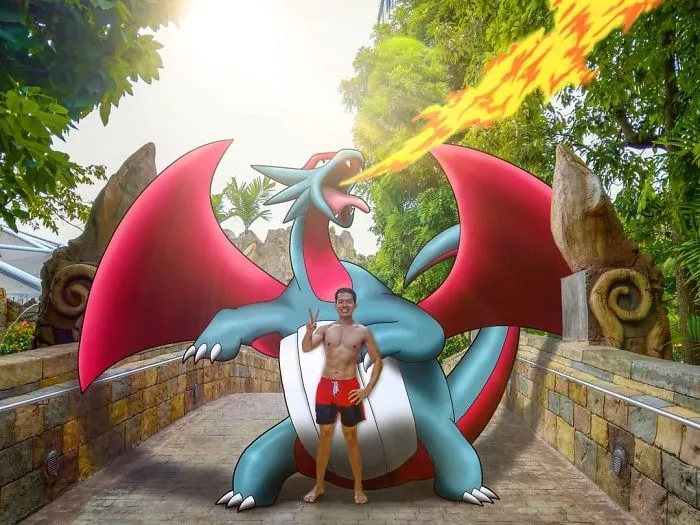 Man posing with a fire-breathing Pokémon illustration on a scenic pathway.