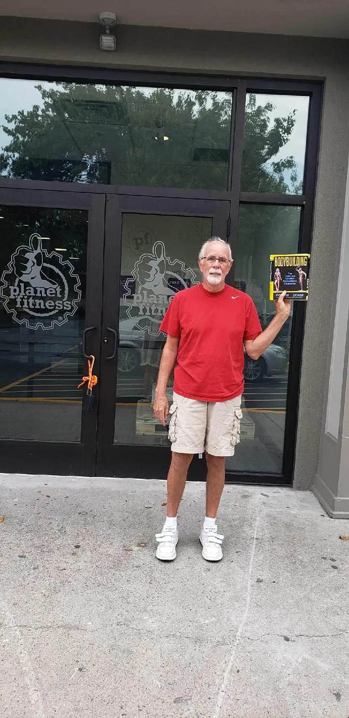 Frente a un gimnasio, con un libro de culturismo