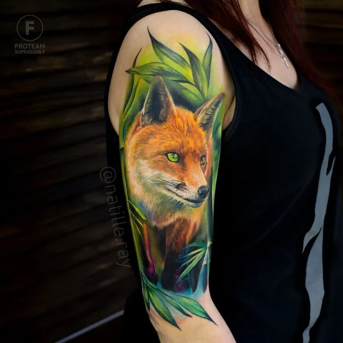Colorful and bright animal tattoo depicting a fox with greenery on a person's upper arm.