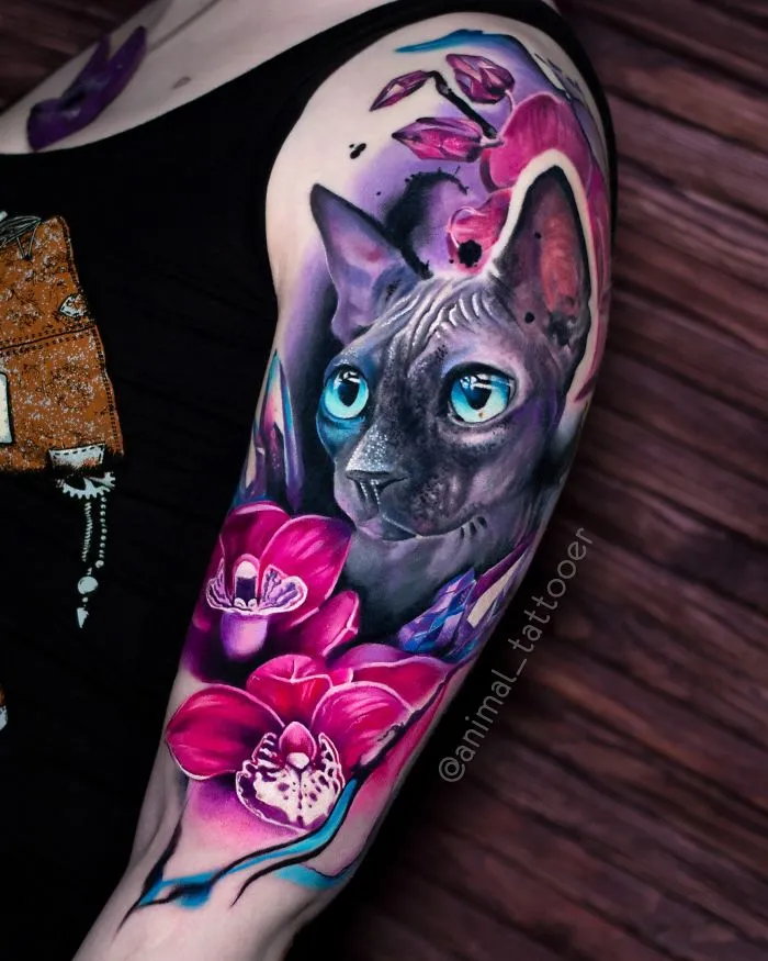 Colorful animal tattoo of a cat with blue eyes and pink flowers on arm.