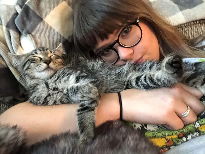 Woman wearing glasses cuddling a relaxed tabby cat, showcasing a wholesome rescue pet photo moment.