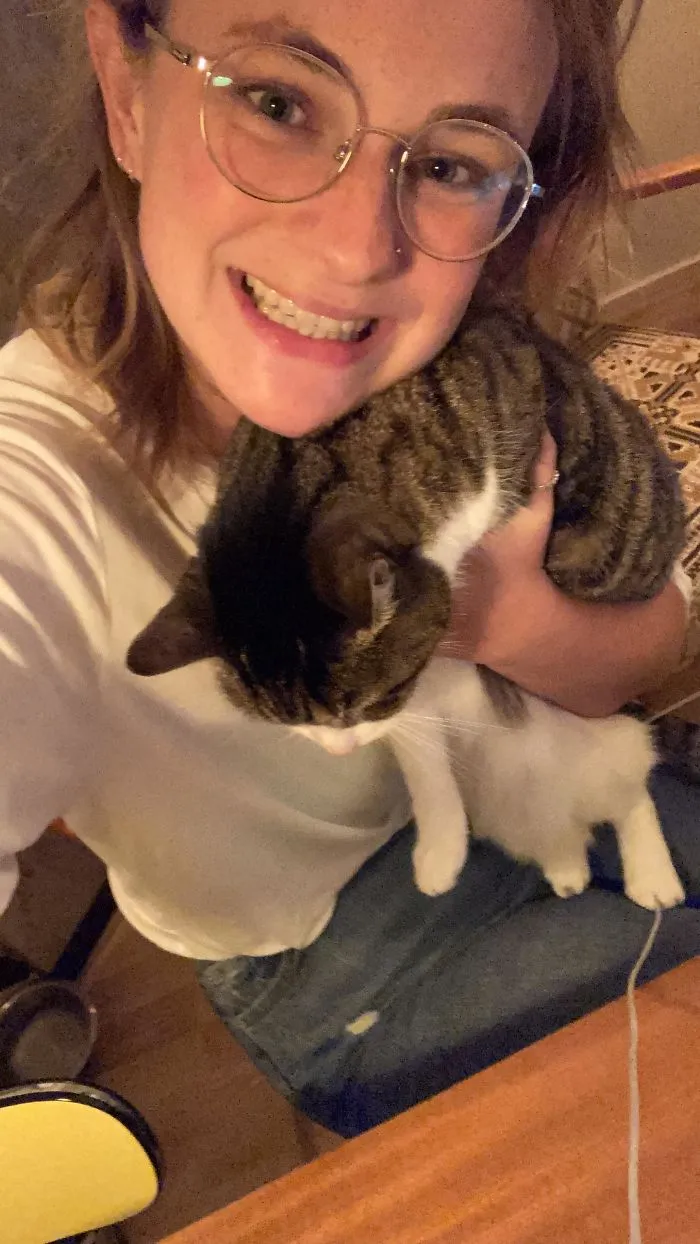 Smiling woman wearing glasses holds a relaxed tabby and white cat in a cozy indoor setting, showcasing rescue pet affection.