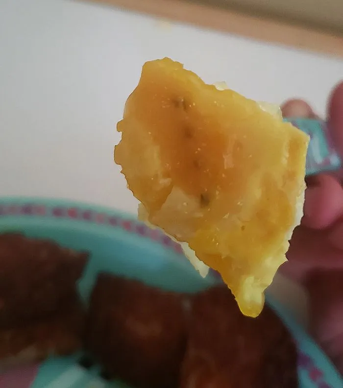 A close-up of a fork holding a piece of scrambled egg with a plate of food in the background, showing kids are not born smart.
