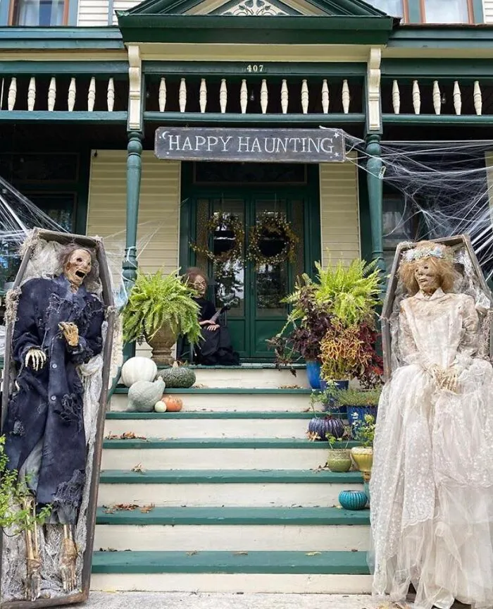 Halloween decorations on a porch with skeletons in coffins, pumpkins, and a happy haunting sign, spooky and funny.