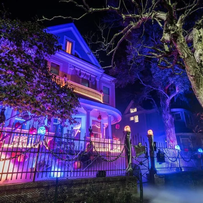 Halloween decorations on a Victorian house with colorful lighting and spooky pumpkin and mask accents at night