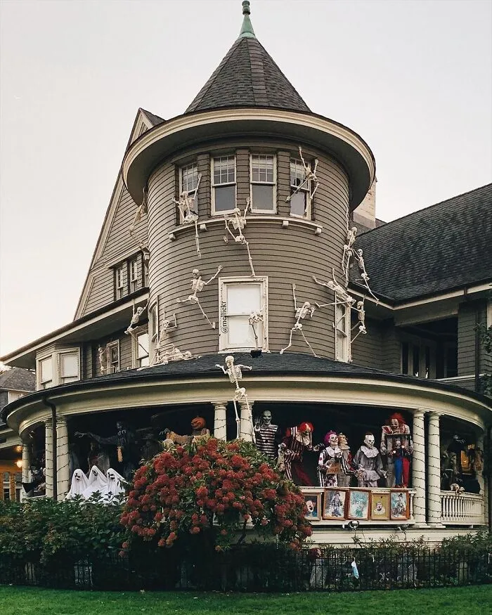 Victorian house with Halloween decorations including skeletons climbing walls and creepy clowns on porch for spooky Halloween decor.