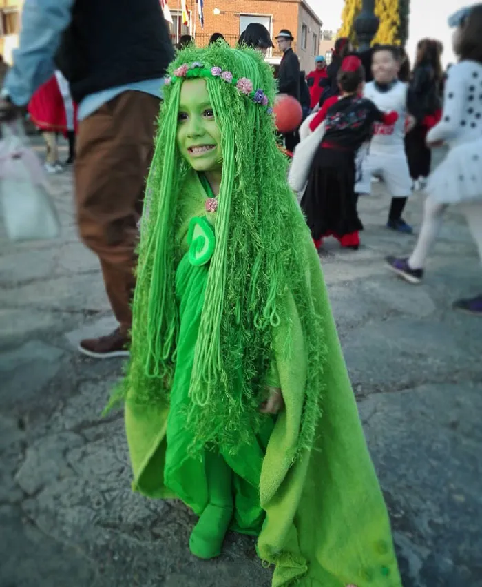 A young child dressed as a forest spirit with green yarn hair for Halloween costumes