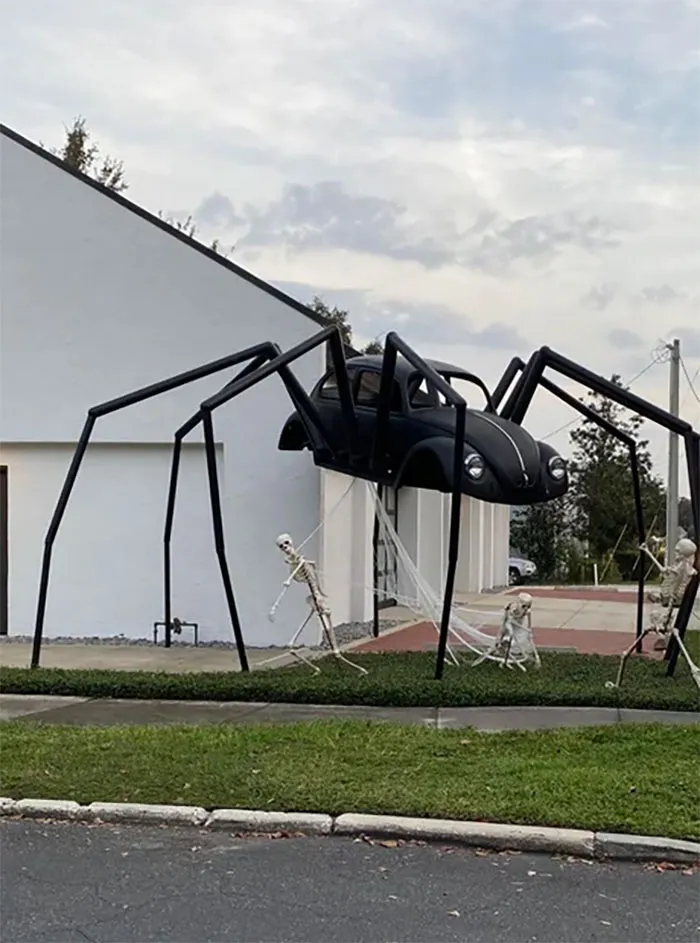 Halloween decorations featuring a giant spider made from a car with skeletons in a yard, both funny and frightening.