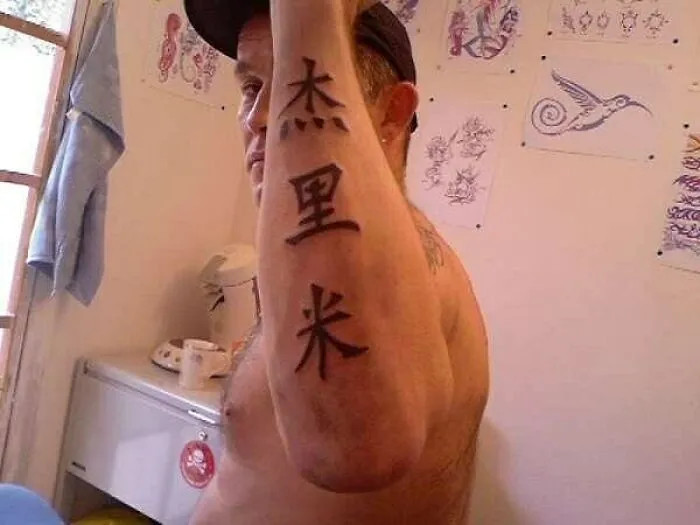 Man with foreign language tattoo, displaying characters on his forearm in a tattoo parlor.