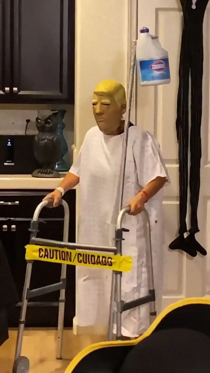 Person in a Trump mask and hospital gown holding a walker as a funny Halloween costume