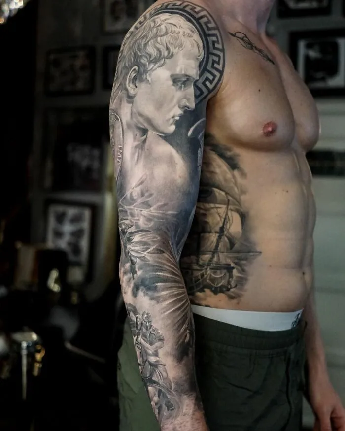 Man showcasing a black and gray realism tattoo sleeve by a Swedish artist, featuring a classical statue design.