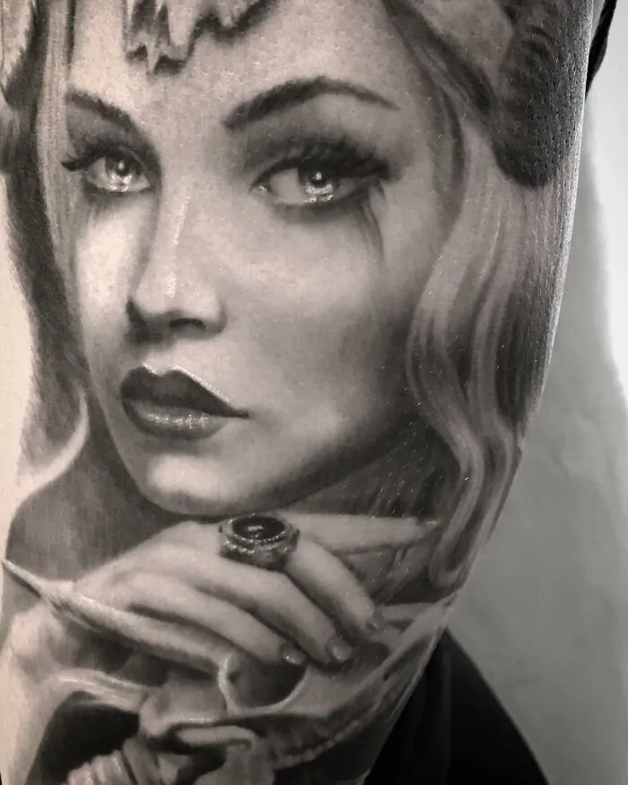 Black and gray realism tattoo of a woman's face by Swedish artist, detailed with ornate jewelry and flowing hair.