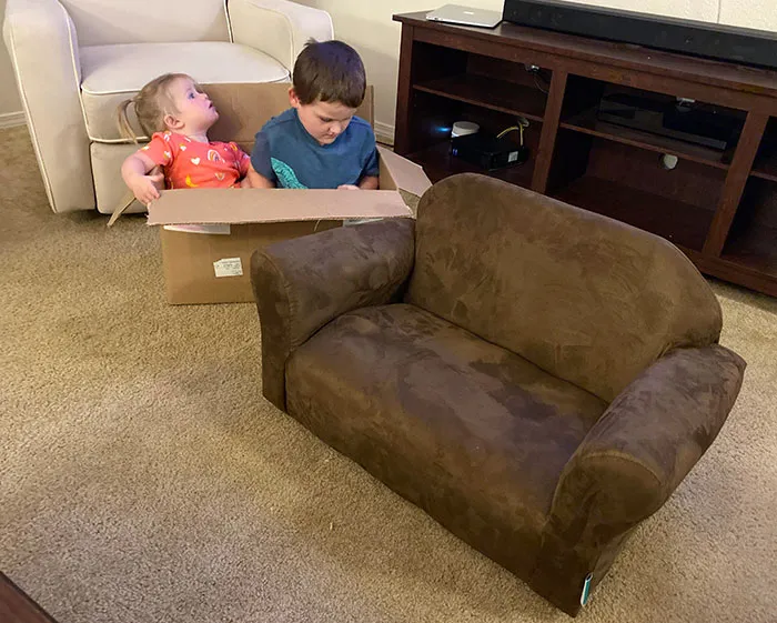 Mis hijos sentados juntos al lado del sofá nuevo que mi esposa les ha comprado