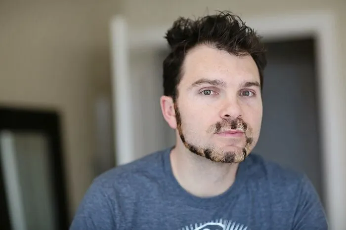 Man with a monkey tail beard wearing a blue shirt, showcasing unique facial hair style.