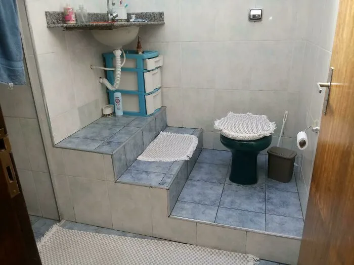 Awkward bathroom interior with steps leading to a sink and toilet, showcasing peculiar design choices.