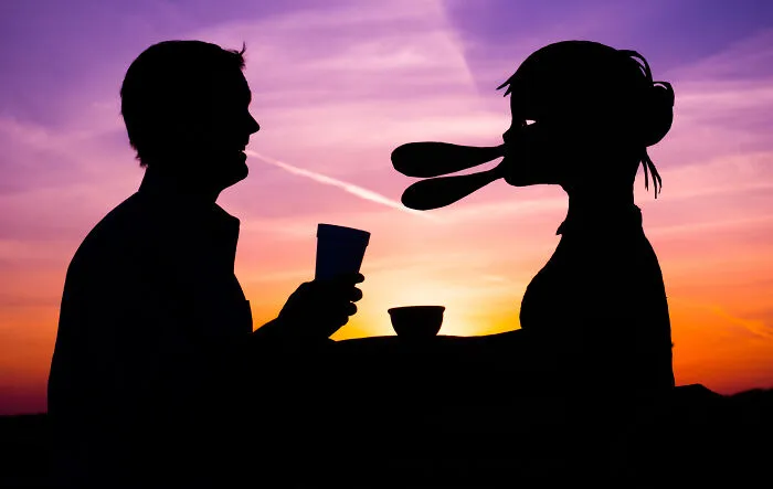 Silhouette of a couple with selfie date cardboard cutouts at sunset, celebrating Valentine's Day mood.