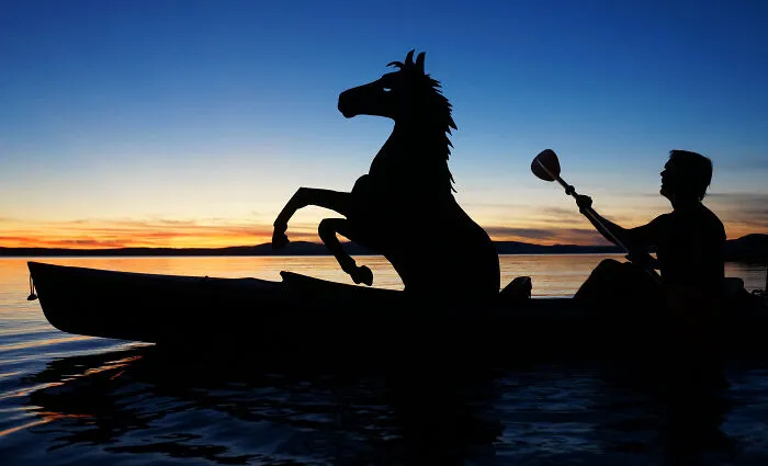 Person kayaking with a cardboard horse cutout at sunset, creating a unique selfie date atmosphere.