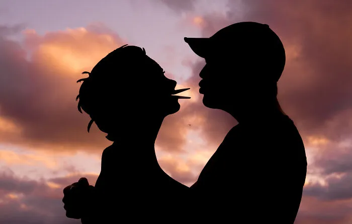 Silhouettes of a couple kissing with a sunset background, featuring Valentine’s Day cardboard cutouts.