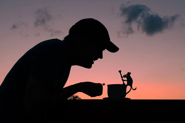 Silhouette of a person with a cardboard cutout of a cat on a cup at sunset, evoking a Valentine’s Day mood.