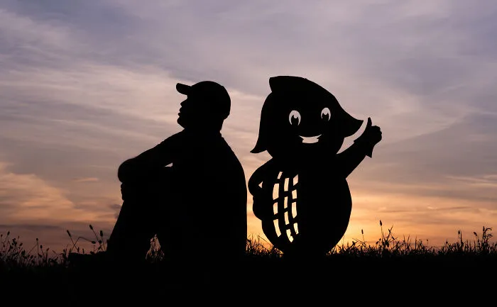 Silhouette of a man sitting beside a smiling cardboard cutout at sunset, depicting a Valentine's Day theme.
