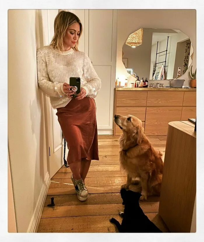 Celebrity posing with two dogs indoors, showcasing love for dogs in a cozy home setting with wooden floors.