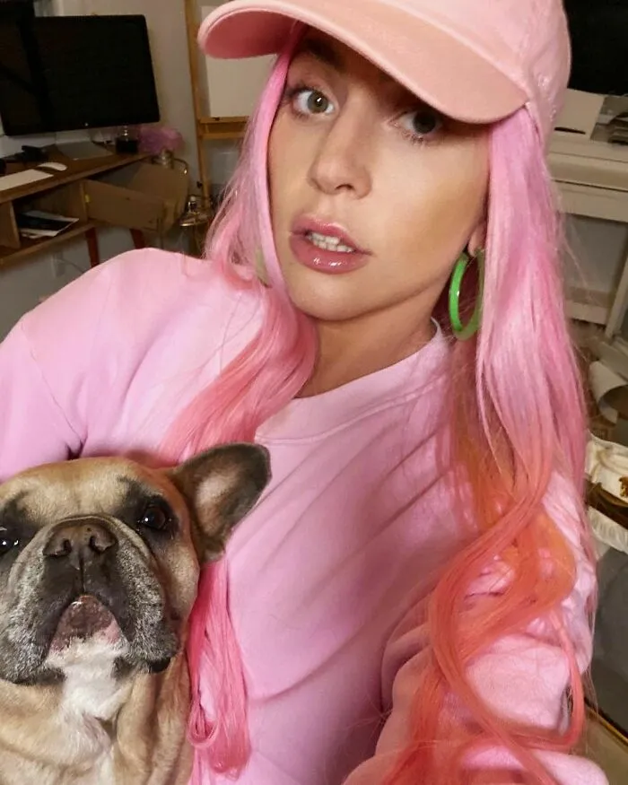 Celebrity with pink hair and green hoop earrings wearing a pink outfit posing with her dog showing love for dogs.