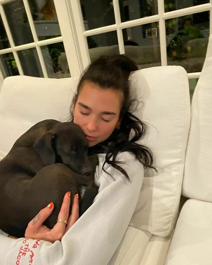 Woman hugging a black dog on a white couch, showing immense love for dogs in a cozy indoor setting.