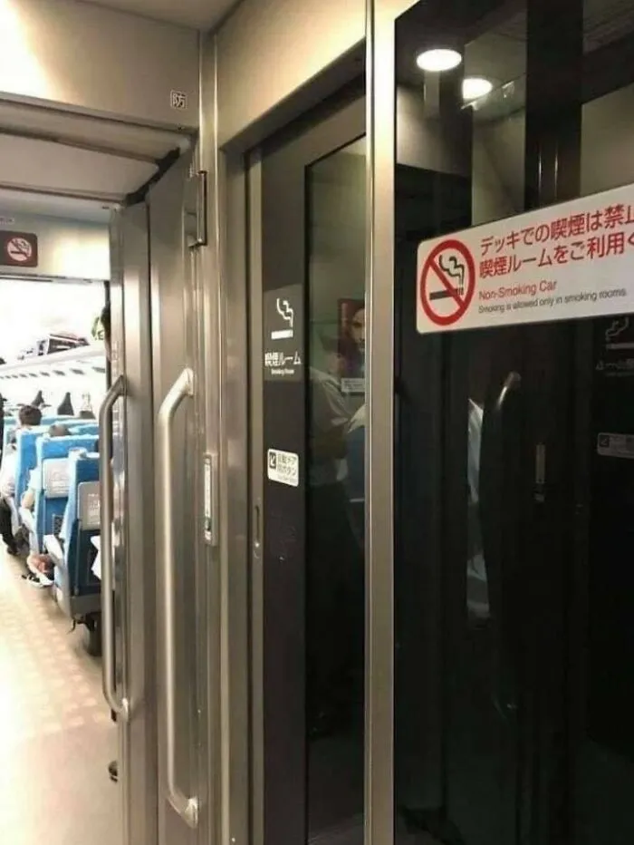 Smoking room on Japanese train, illustrating unique country features, with non-smoking signs and blue passenger seats visible.