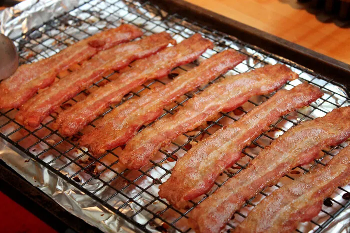 Several cooked bacon strips cooling on a wire rack over a foil-lined baking tray, illustrating conspiracy theories people believe in.