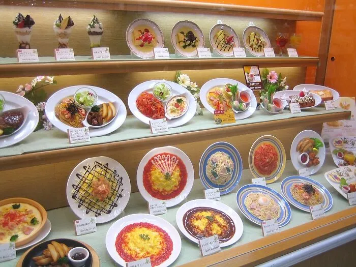 Japanese food display shows intricate plastic replicas of various dishes in a restaurant showcase.