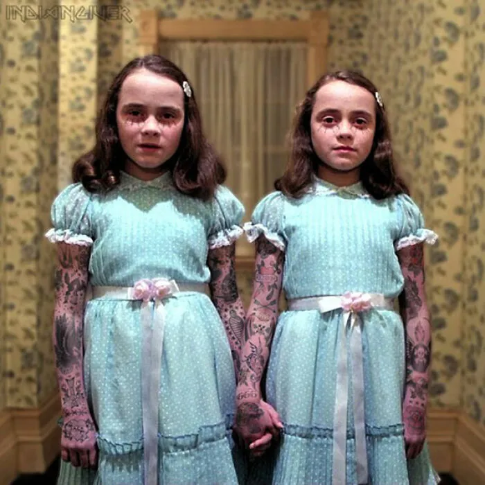 Twin girls in blue dresses with tattoos photoshopped on their arms, standing in a vintage room.