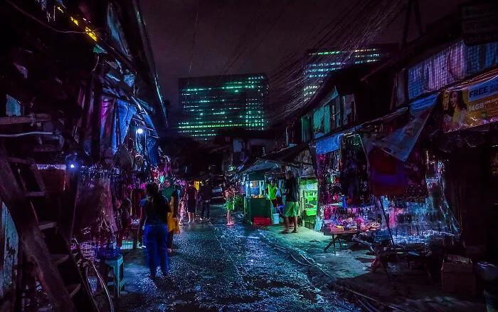 A Street Scene From The Same Slum, With Megacorp-Owned Buildings Towering Over It
