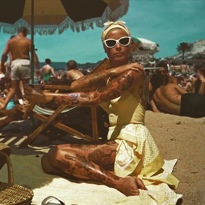 A woman in a yellow dress at the beach, photoshopped tattoos covering her arms and legs, creating a striking contrast.