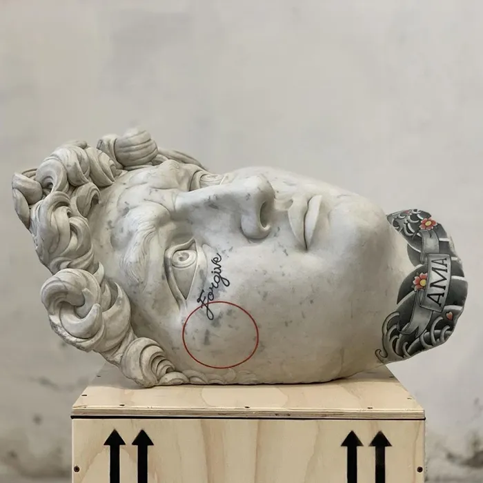Sculpture head with tattoos by Italian artist, showcasing designs on stone instead of skin.